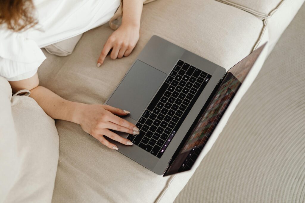 Close-up of a person working from home on a laptop, comfortable on a beige couch.