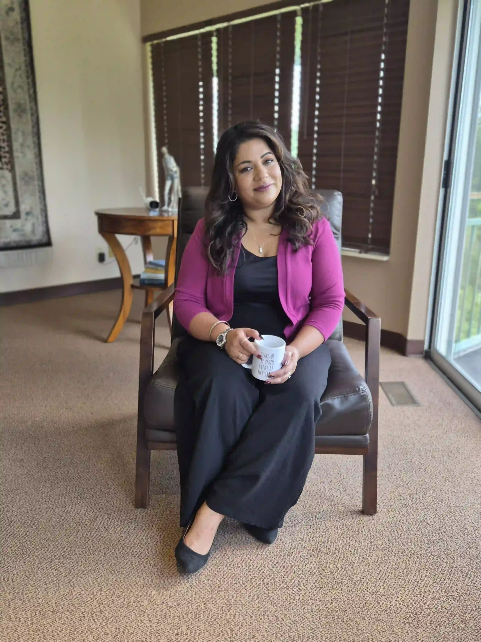 Anam Tareen seated beside an office window in a magenta cardigan.